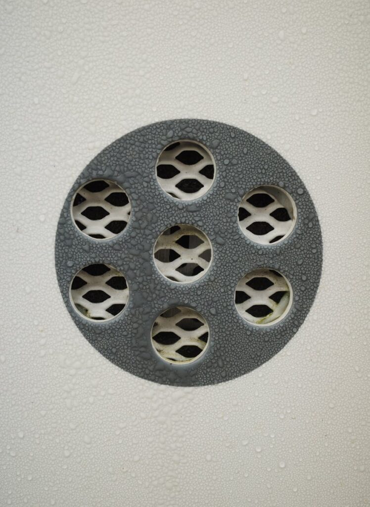 Detailed view of a wet metal drain cover with water droplets and textured surface.