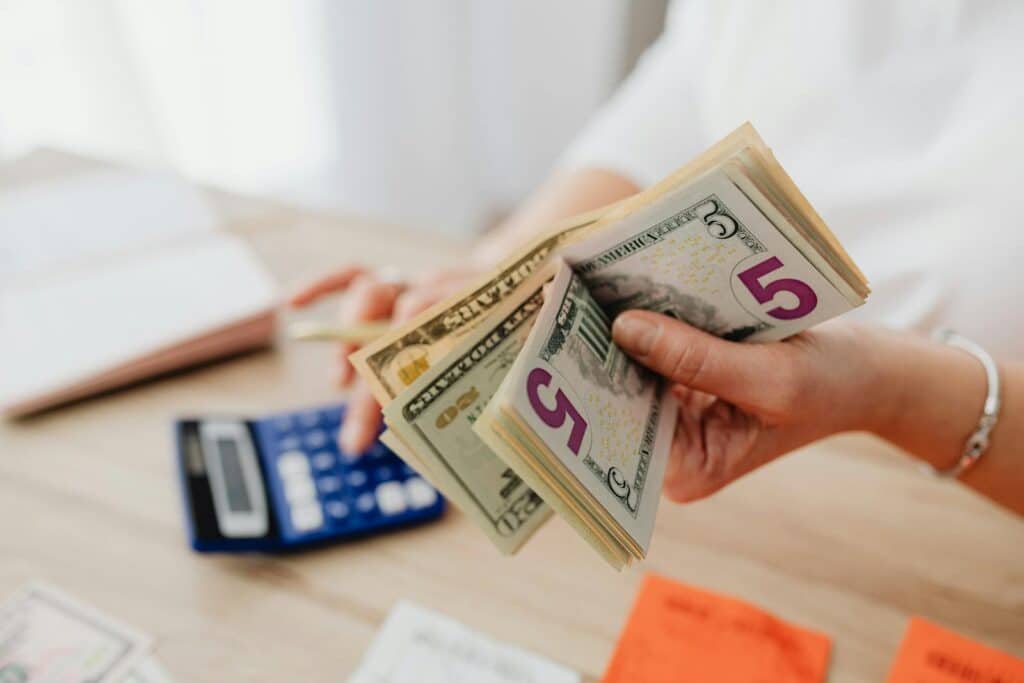 Close-up of hands counting US dollar bills with a calculator, highlighting finance and savings.