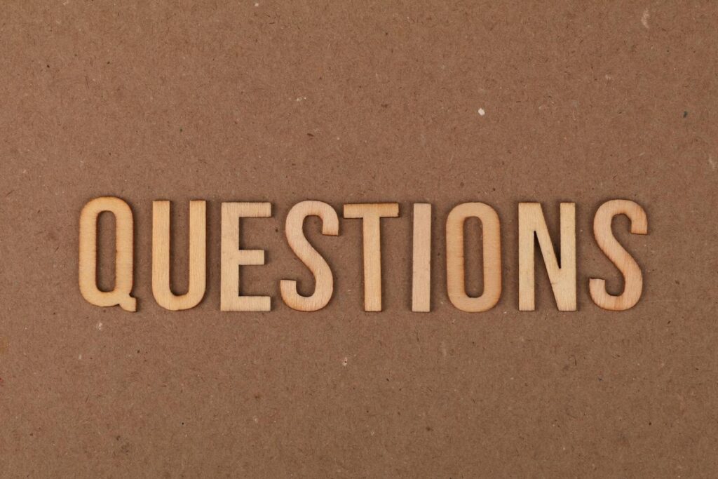 Wooden letters spelling the word "QUESTIONS" on a cardboard background, providing a neutral copyspace.