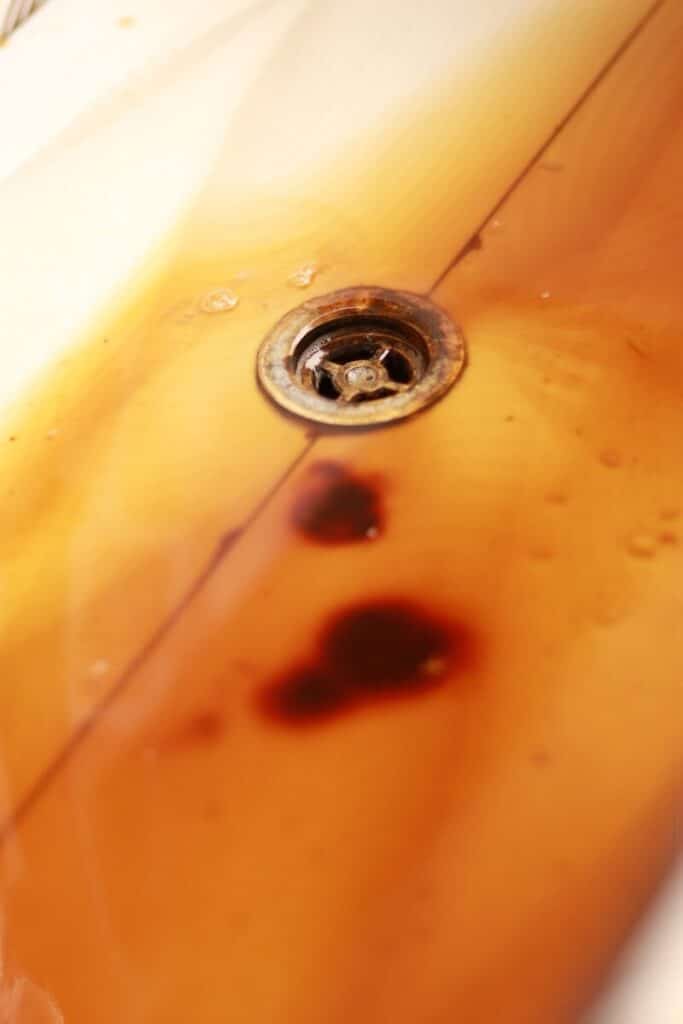 Close-up of a rusty drain in a dirty, stained bathtub.